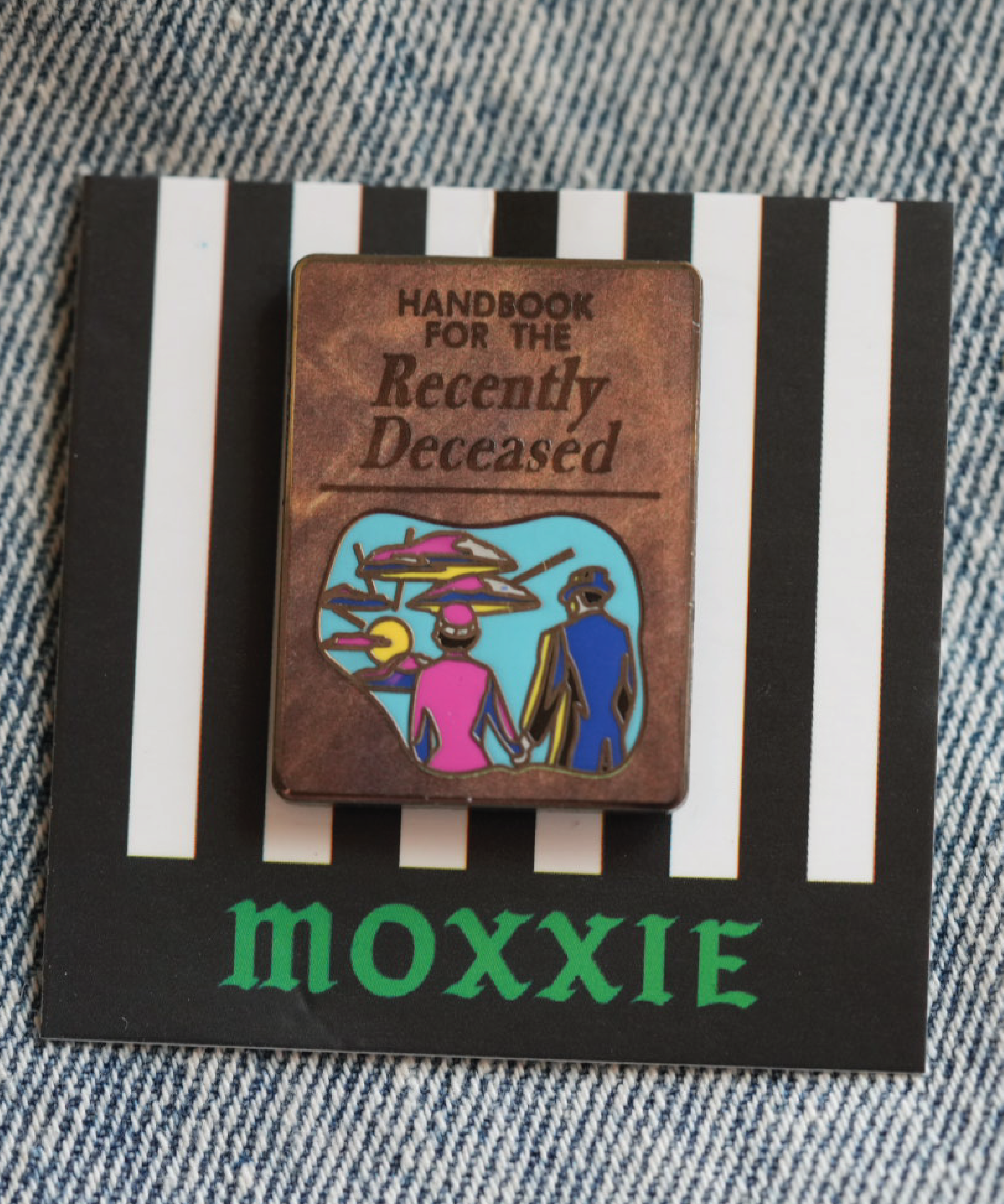 A spooky Beetlejuice-inspired enamel pin featuring the iconic Handbook for the Recently Deceased, perfect for any horror fan.