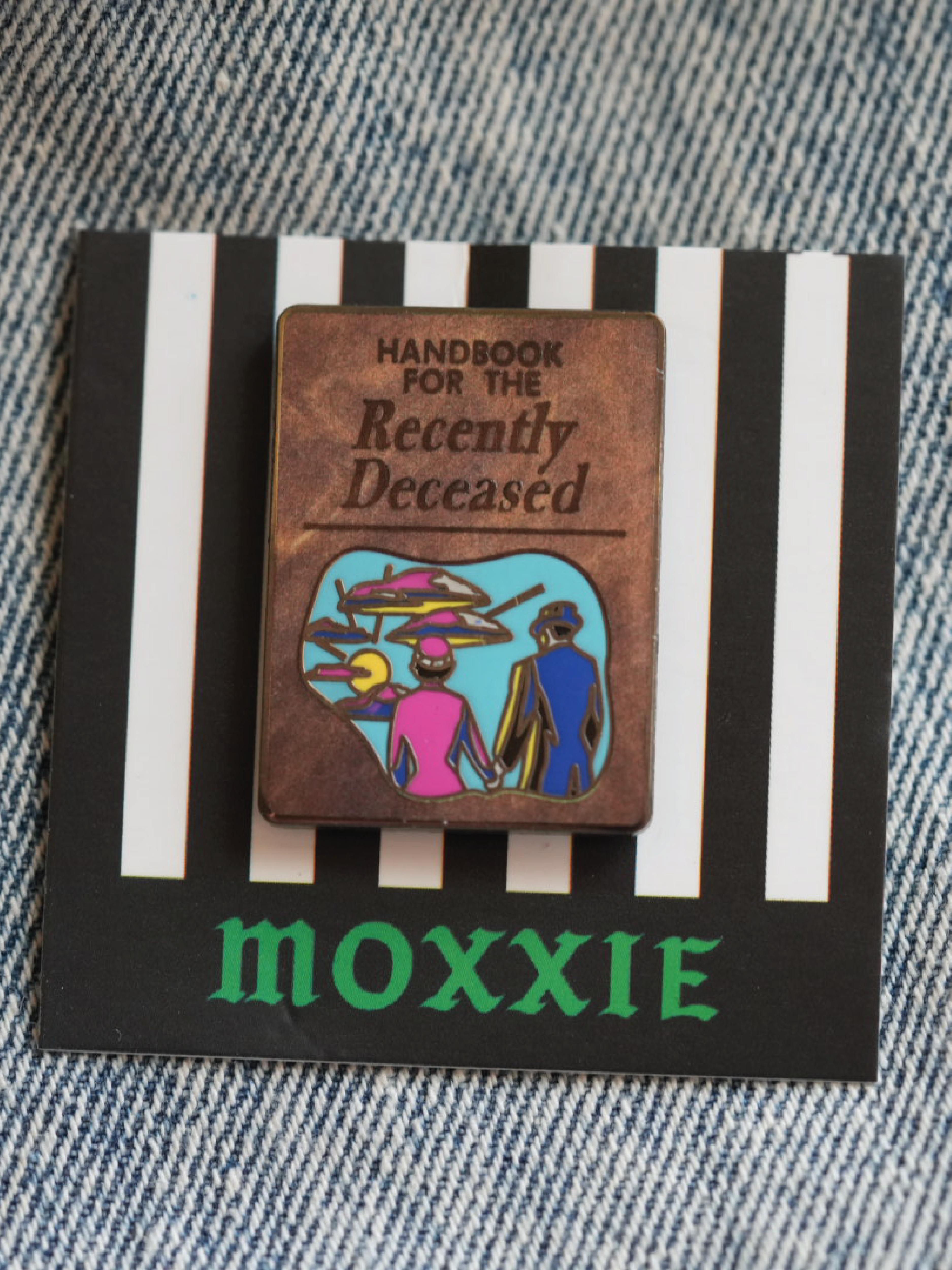 A spooky Beetlejuice-inspired enamel pin featuring the iconic Handbook for the Recently Deceased, perfect for any horror fan.