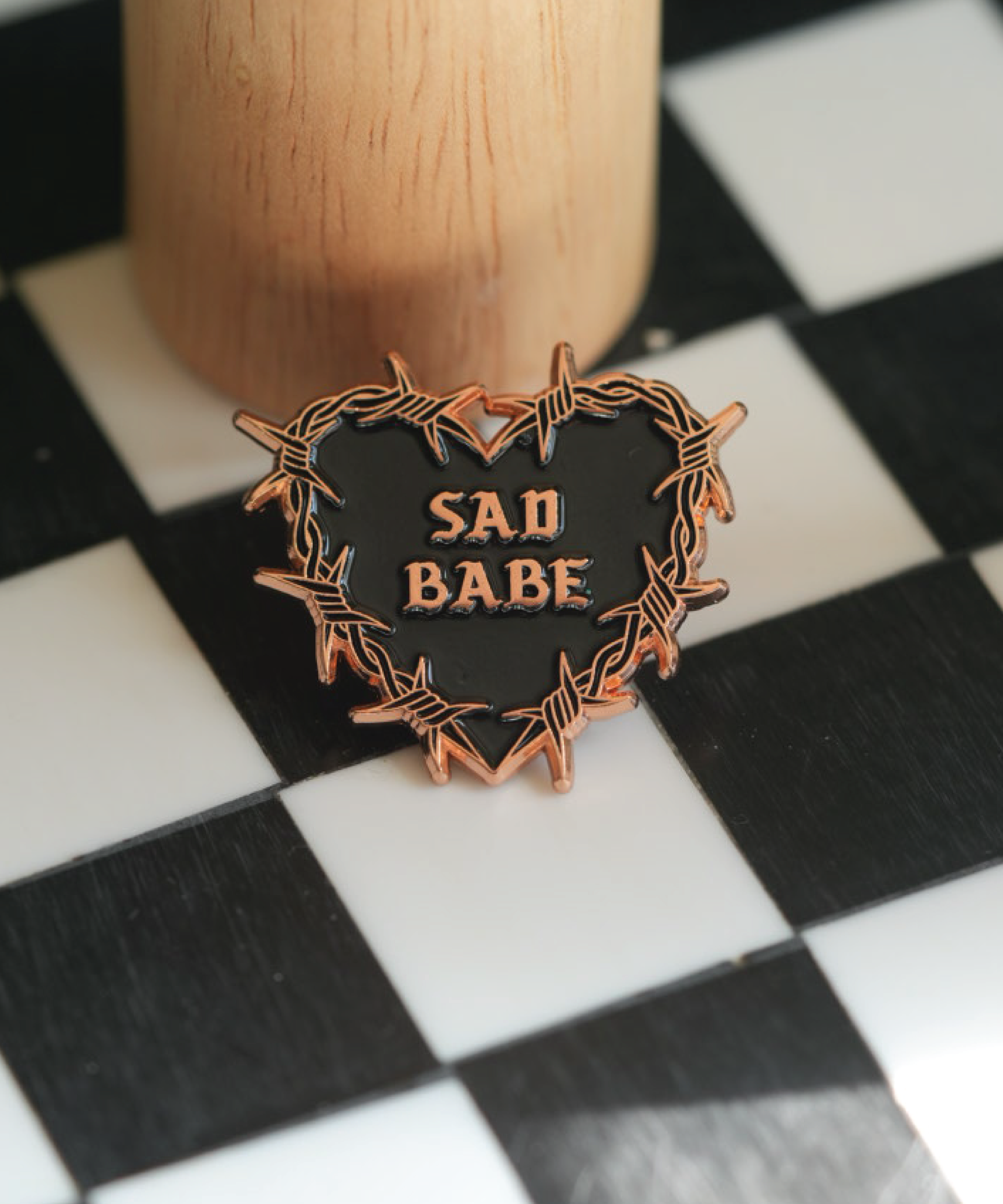 This Sad Babe Copper pin features a barbed wire heart and traditional tattoo design, perfect for adding an emo touch to your pin collection.