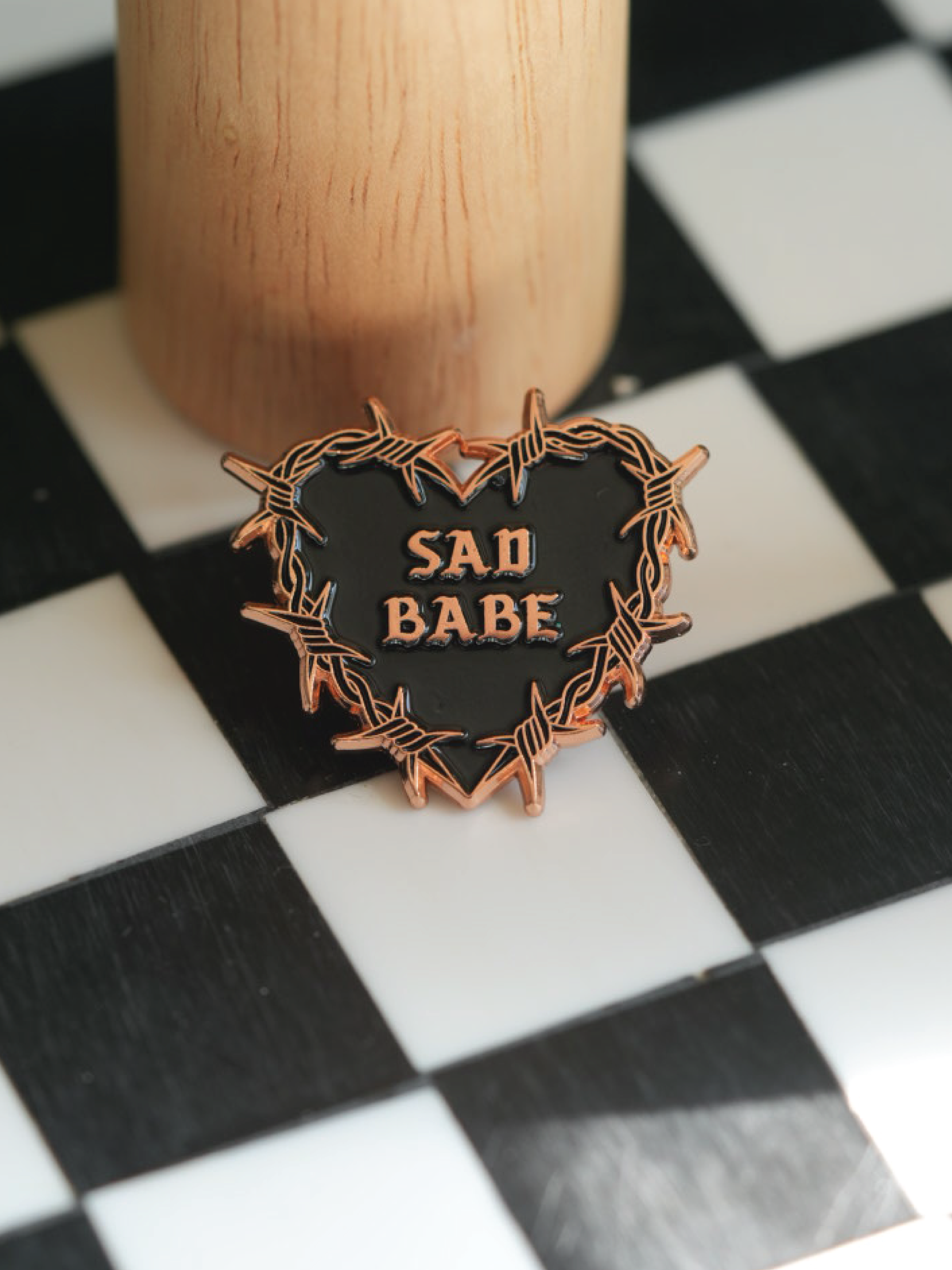 This Sad Babe Copper pin features a barbed wire heart and traditional tattoo design, perfect for adding an emo touch to your pin collection.