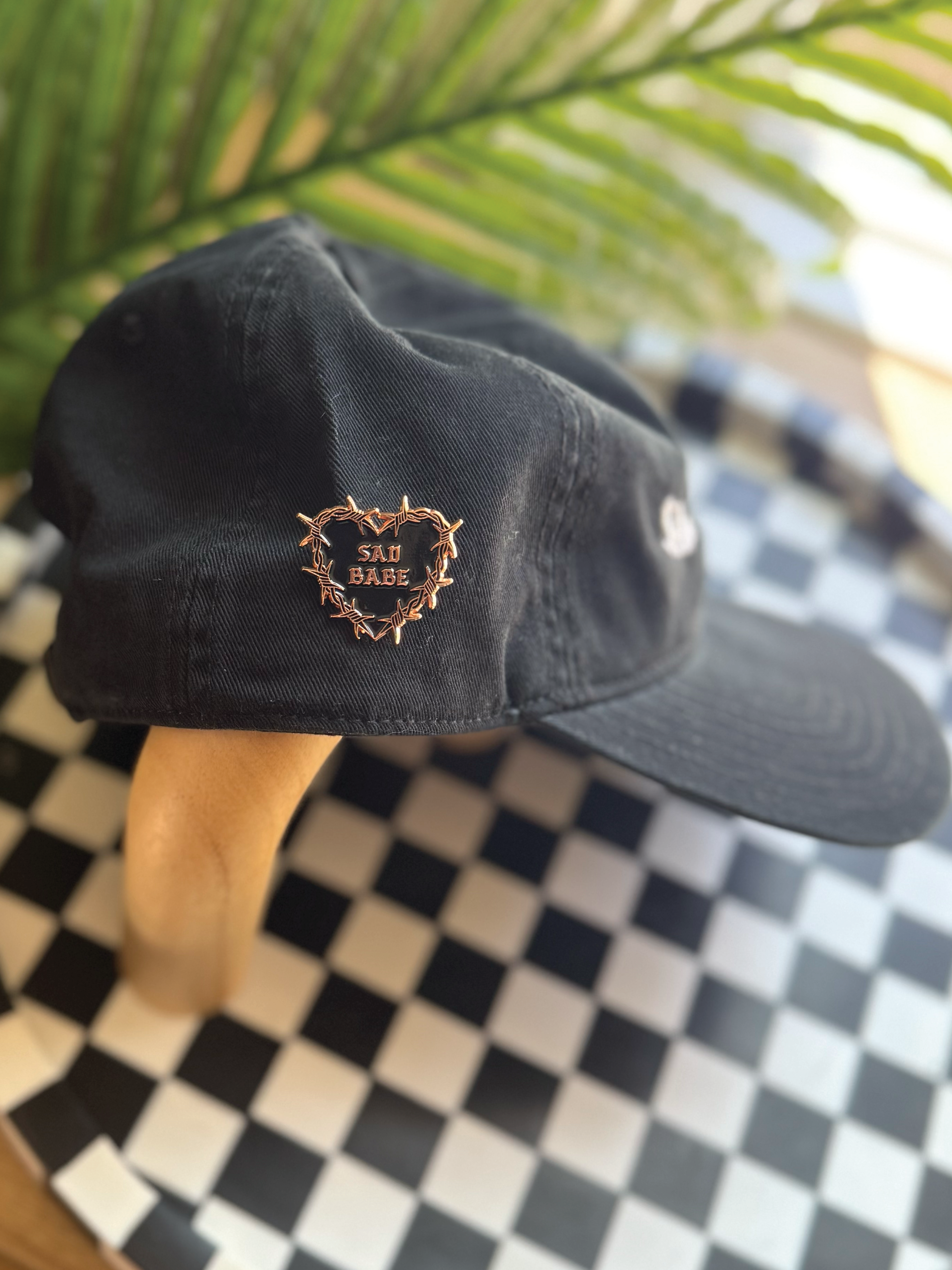 Sad Babe pin with a barbed wire heart and traditional tattoo design adds an edgy, emo touch to a Sad Diego Hat.