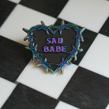 This Sad Babe pin features a barbed wire heart in rainbow metal, blending traditional tattoo style. 