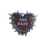 Add a metallic rainbow of color to your pin collection with this Sad Babe pin, featuring a barbed wire heart in rainbow metal and a traditional tattoo design.