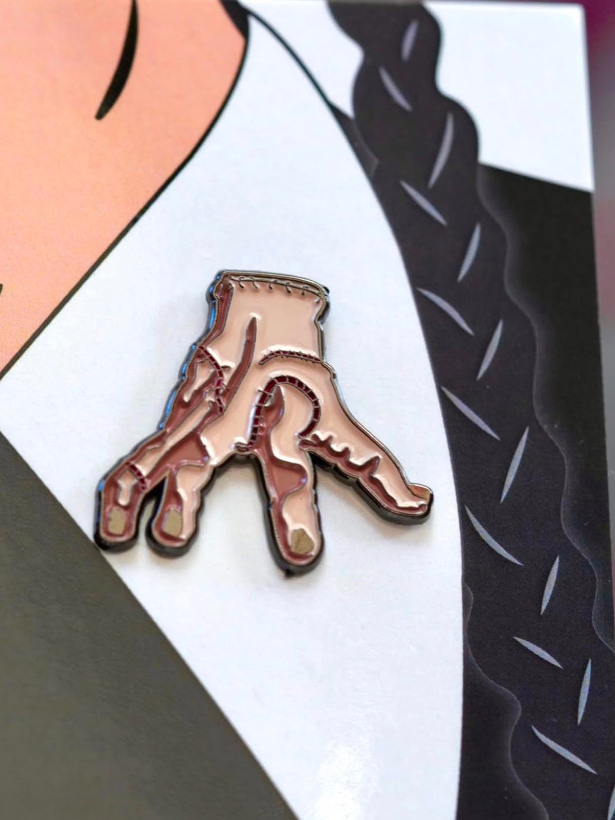 This Wednesday Addams pin set adds a touch of horror to your Halloween look, perfect for any spooky babe. Close up image of the "Thing".