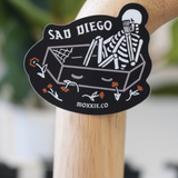 Black 'Sad Diego Gothic' sticker featuring a white skeleton in a coffin, evoking a dark, gothic aesthetic.
