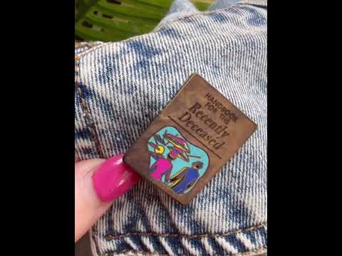 Watch as this spooky Beetlejuice-inspired enamel pin featuring the Handbook for the Recently Deceased adds a haunting touch to a denim jacket, perfect for any horror and Beetlejuice fan.